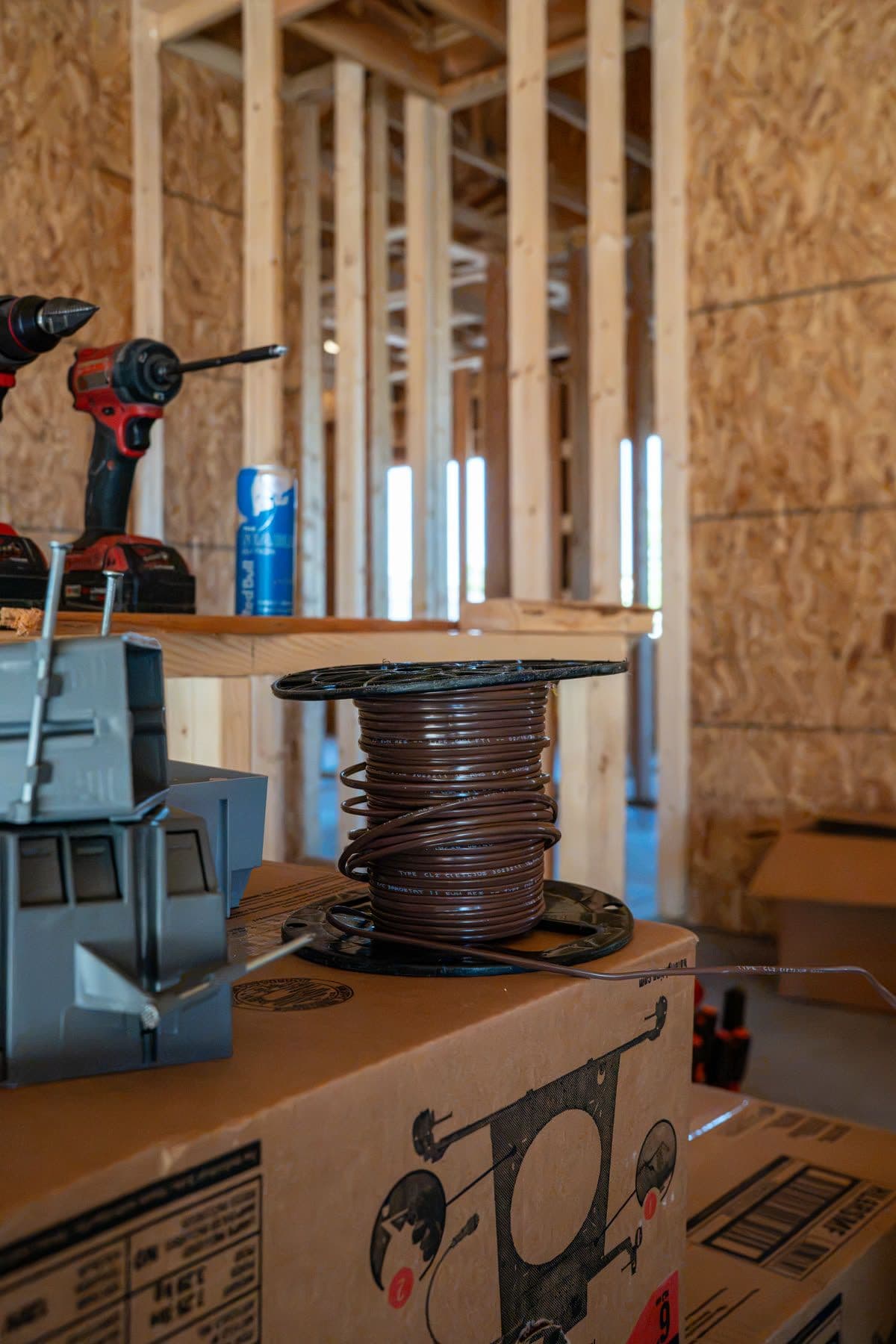 New electrical boxes and a spool of wire on a box at a job site, a drill on the shelf behind