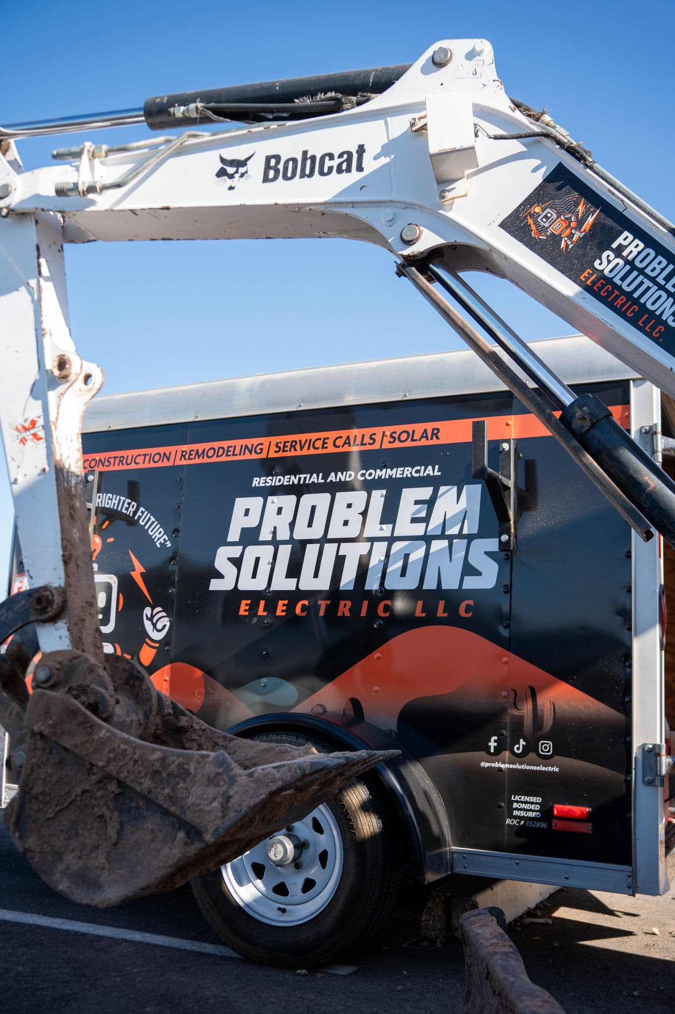 The bucket of the company mini excavator in front of the branded trailer