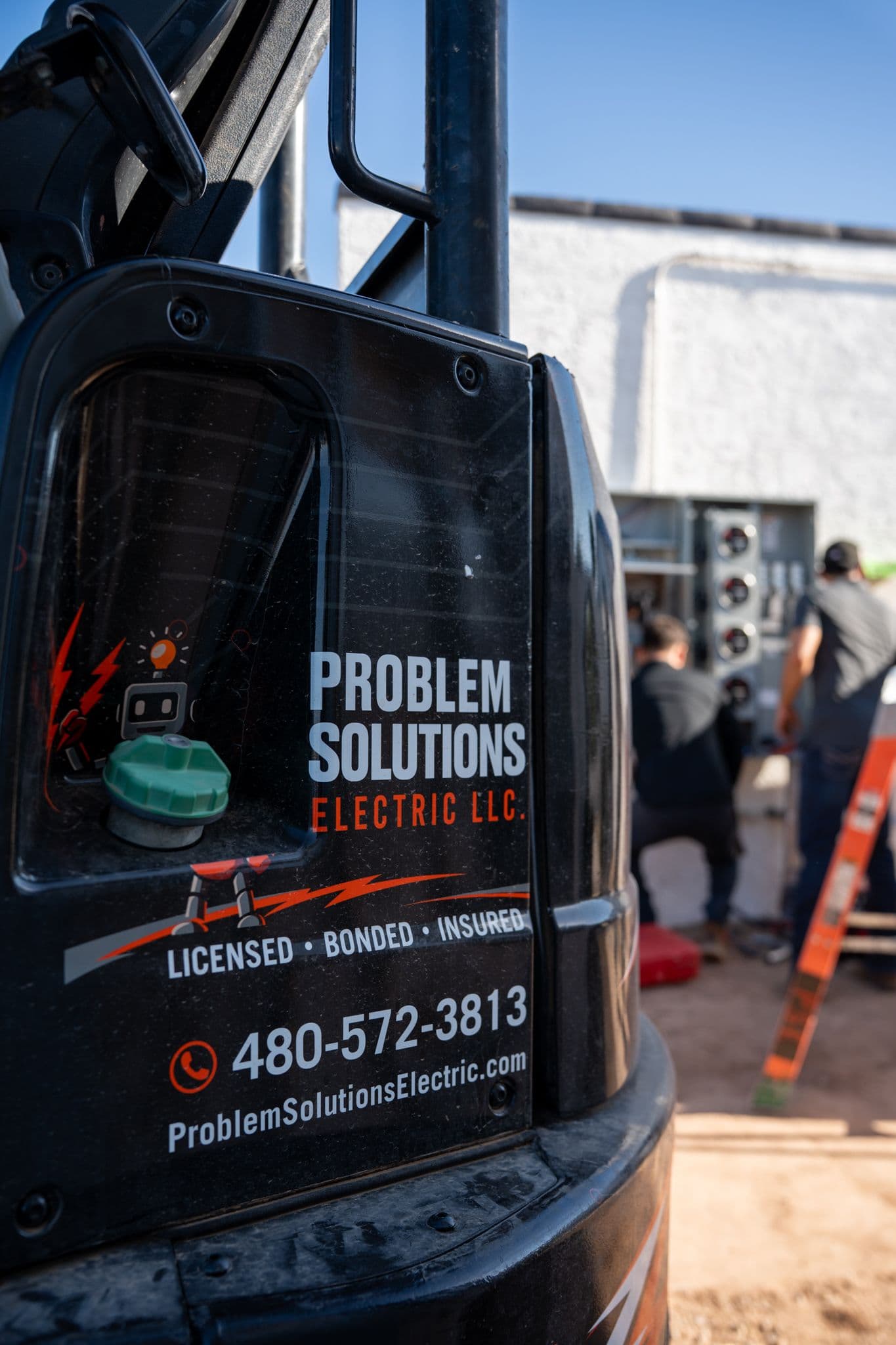 Company logo decal on an excavator cab, with two technicians working at a meter stack behind it