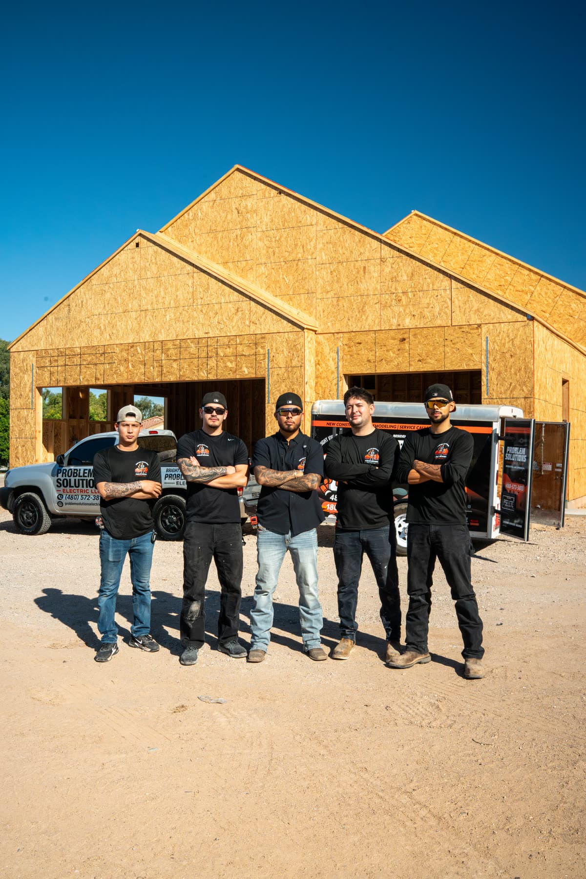 Five crew members in company shirts in front of a framed new house, a company truck behind them