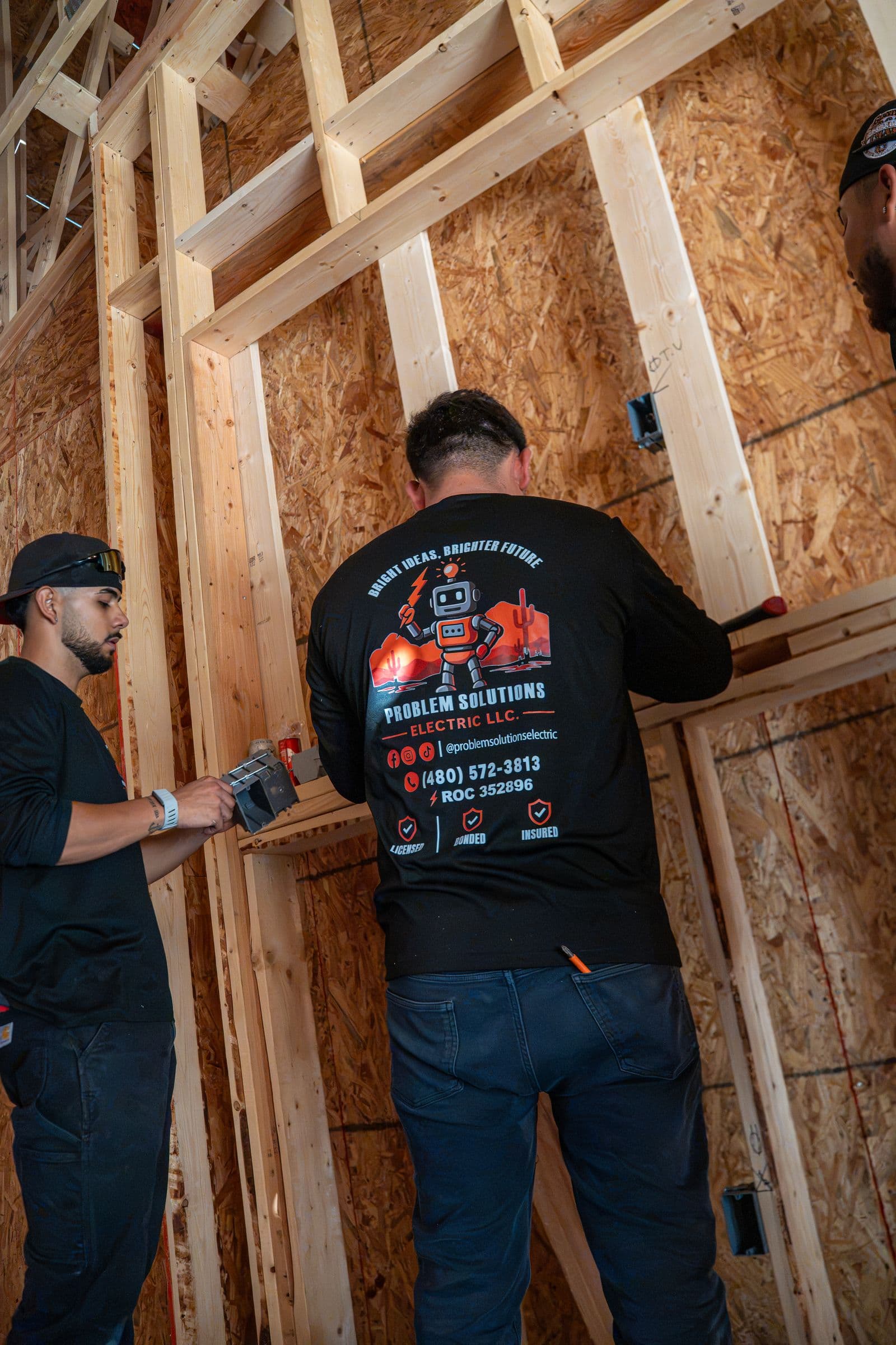 A technician in a company shirt setting a box at a framed opening, a second tech beside him