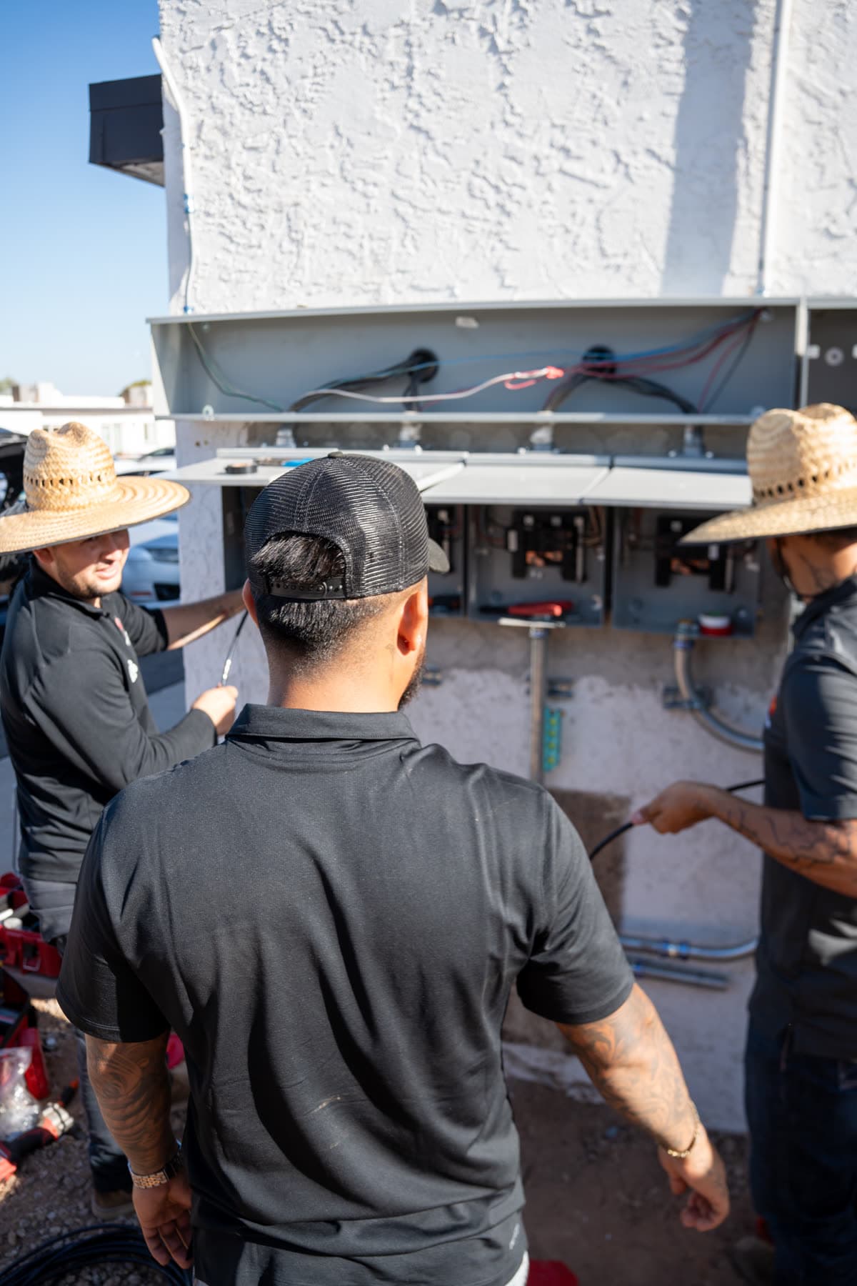 A technician in a cap at a row of open panels, two crew members working beside him