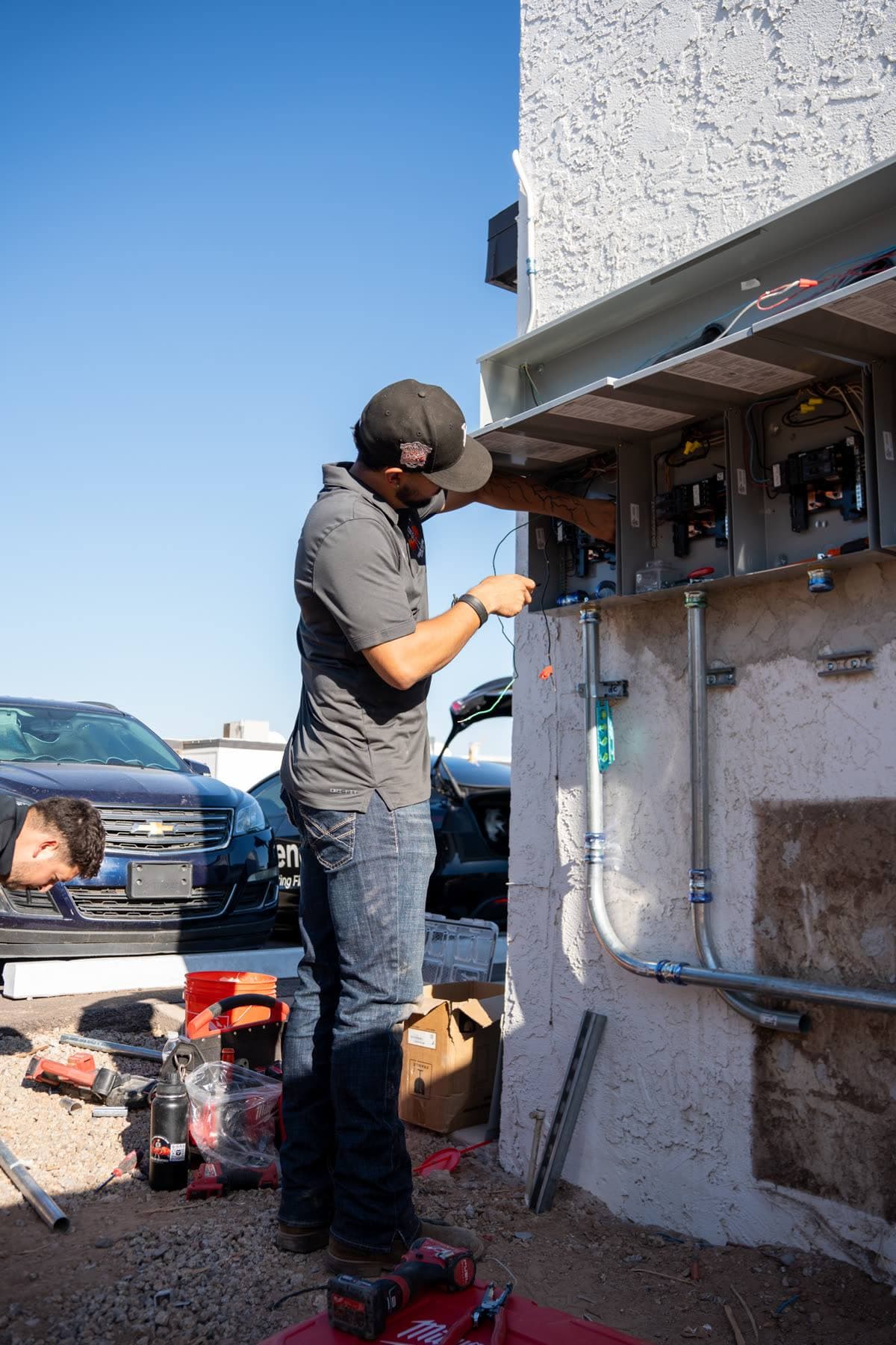 A technician working at a row of open panels on a stucco wall, blue sky behind