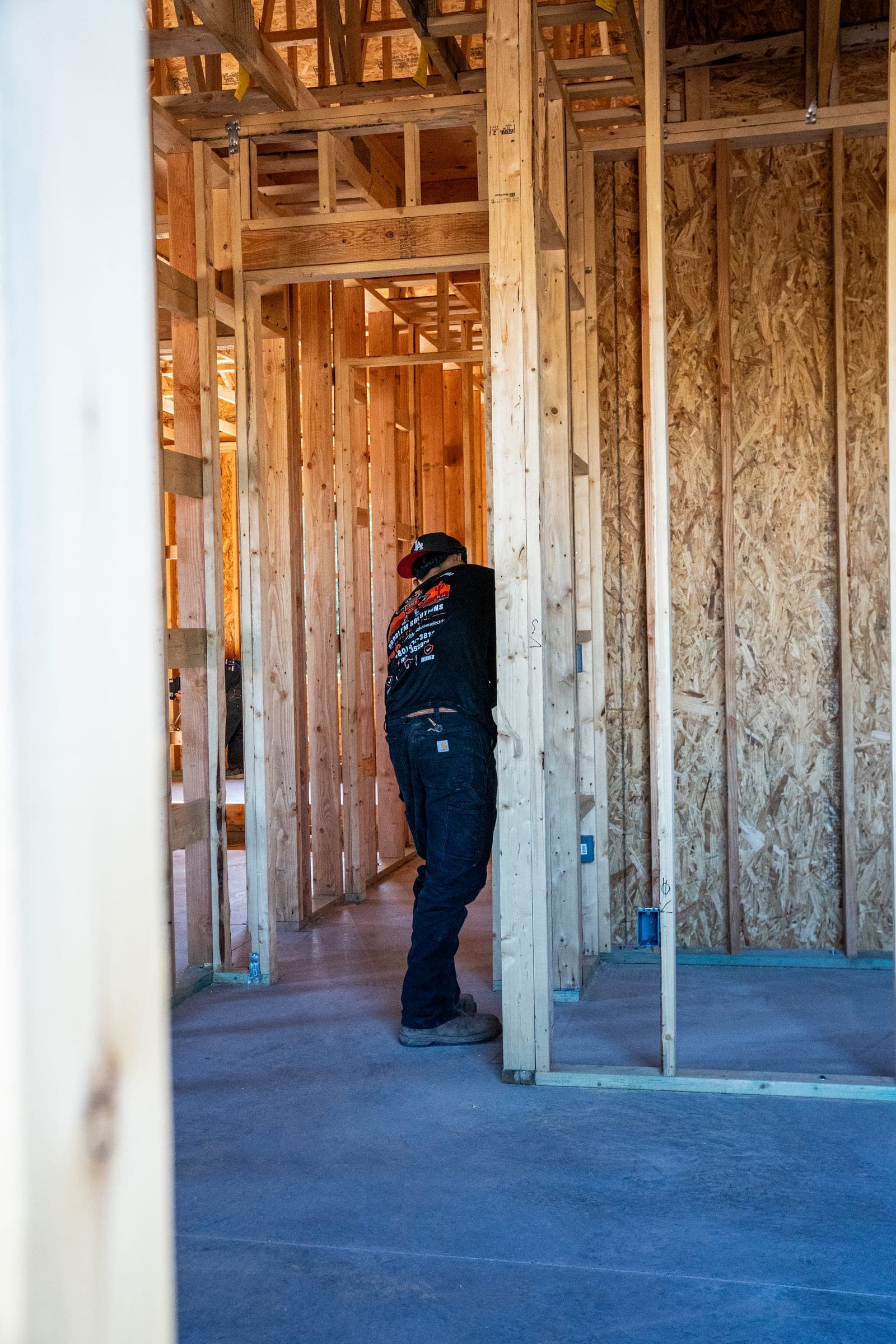 A technician in a logo shirt walking through the framed hallway of a new house