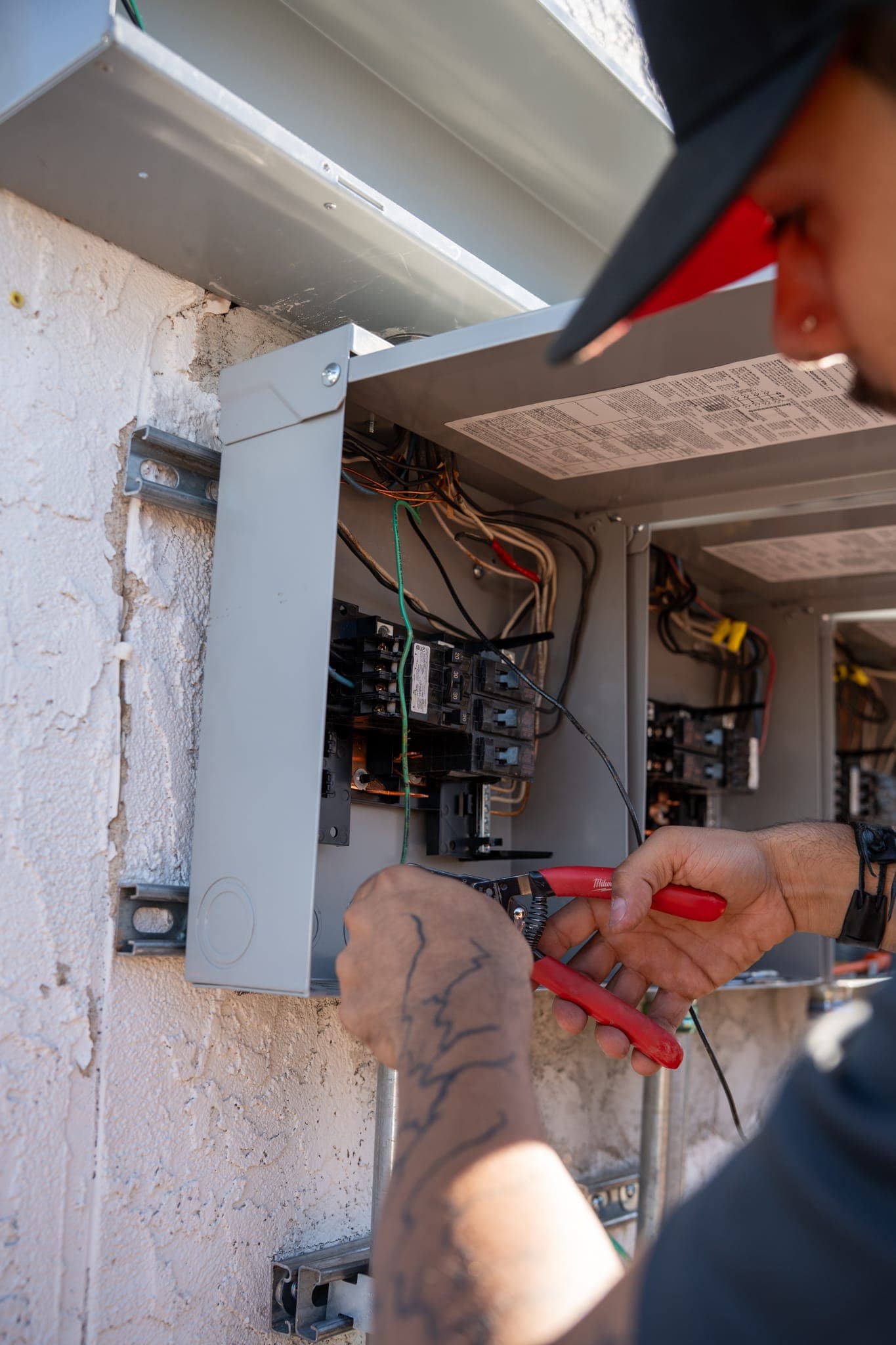 A technician working with wire strippers at the wiring inside an open panel