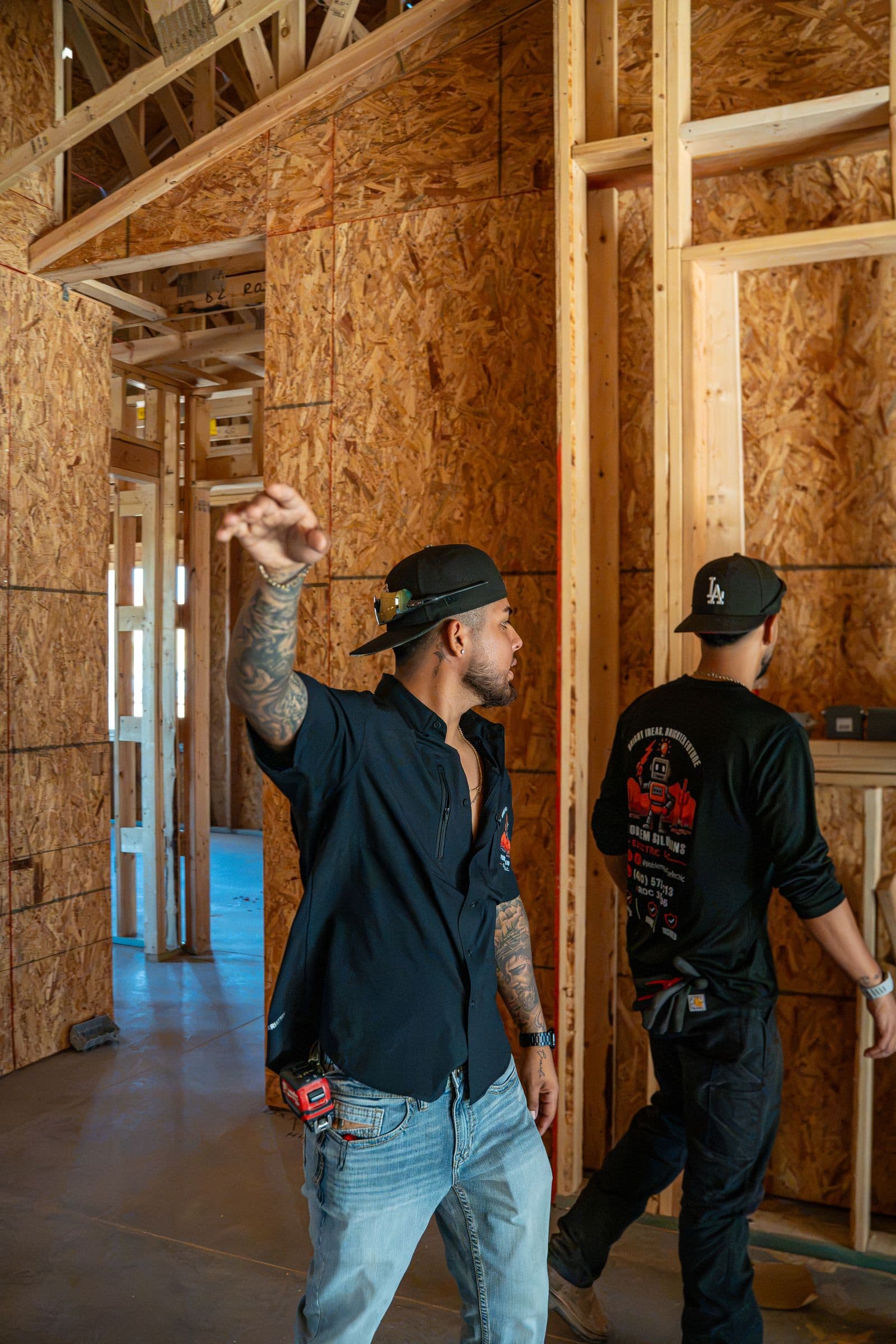 A technician gesturing up at the framing while a second technician looks on