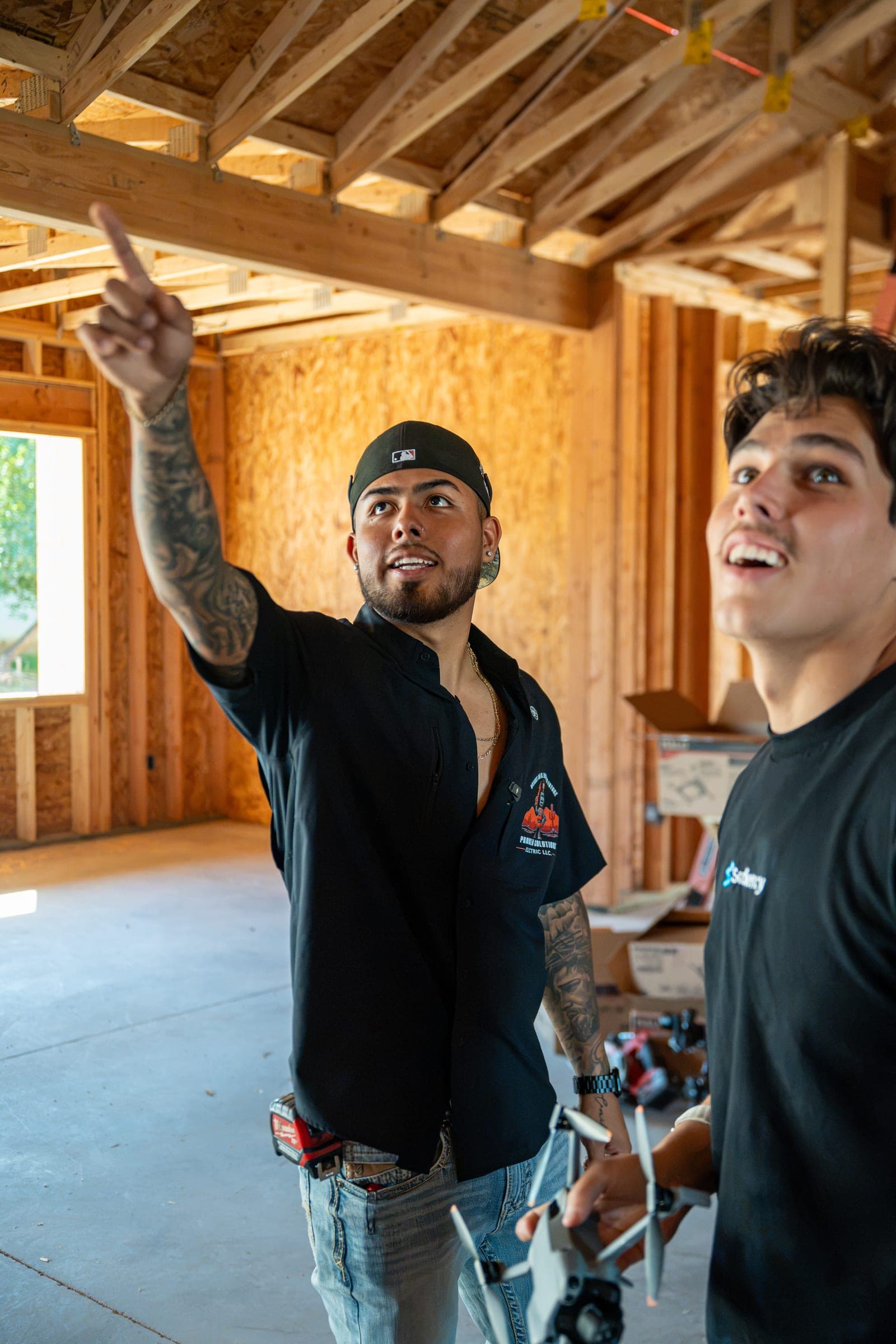 Two technicians in a framed room, one pointing up at the ceiling framing