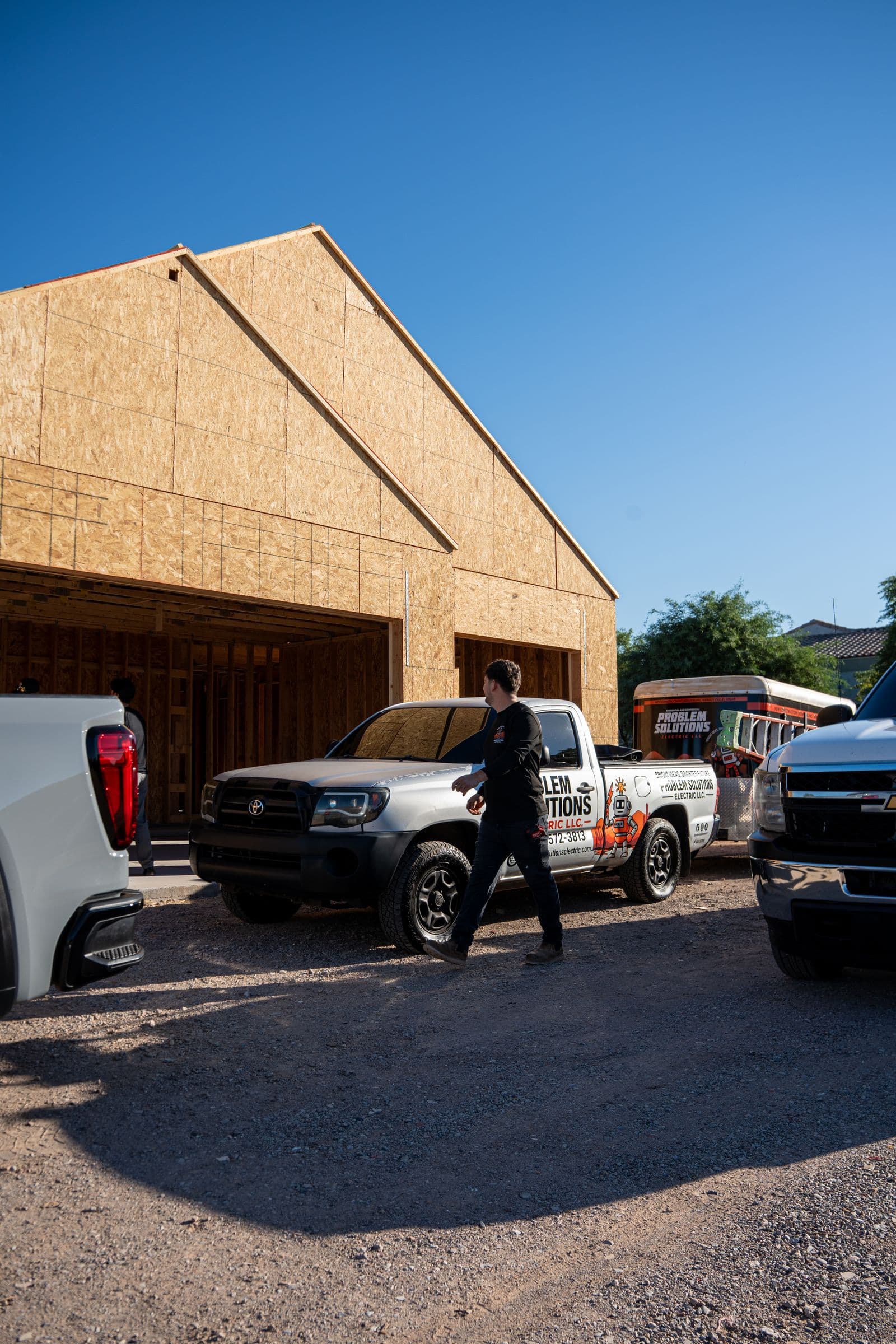A technician walking past a company pickup and trailer at a framed new house